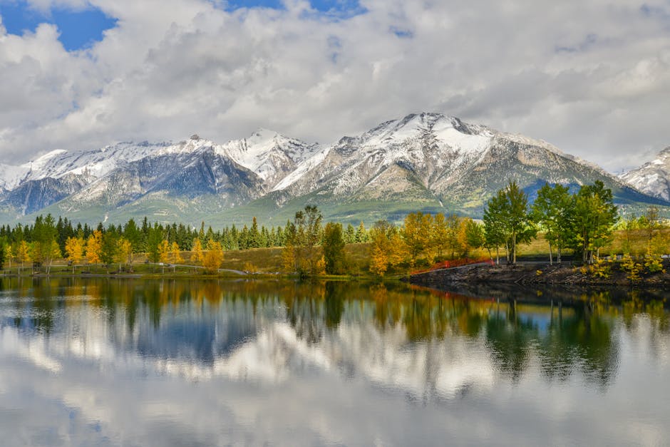 A serene autumn view of Canmore's snowy mountains reflecting in a calm lake.