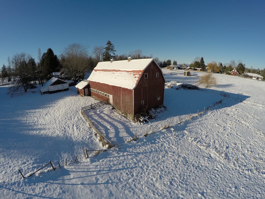 Aerial view of a red barn blanketed in snow under clear blue skies in Langley, BC, Canada.