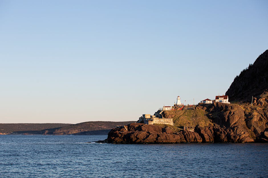Scenic view of a lighthouse perched on cliffs by the sea at sunset, Newfoundland, Canada.