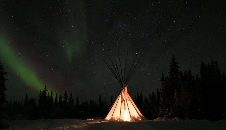 Stunning aurora borealis illuminating a teepee under a starry sky in Yellowknife, Canada.