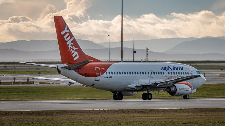 Air North passenger aircraft on the runway during sunset with scenic mountain backdrop.