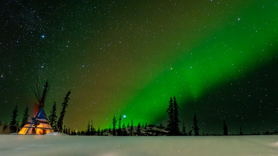 A mesmerizing view of the Northern Lights over a snow-covered Yukon landscape with a teepee.